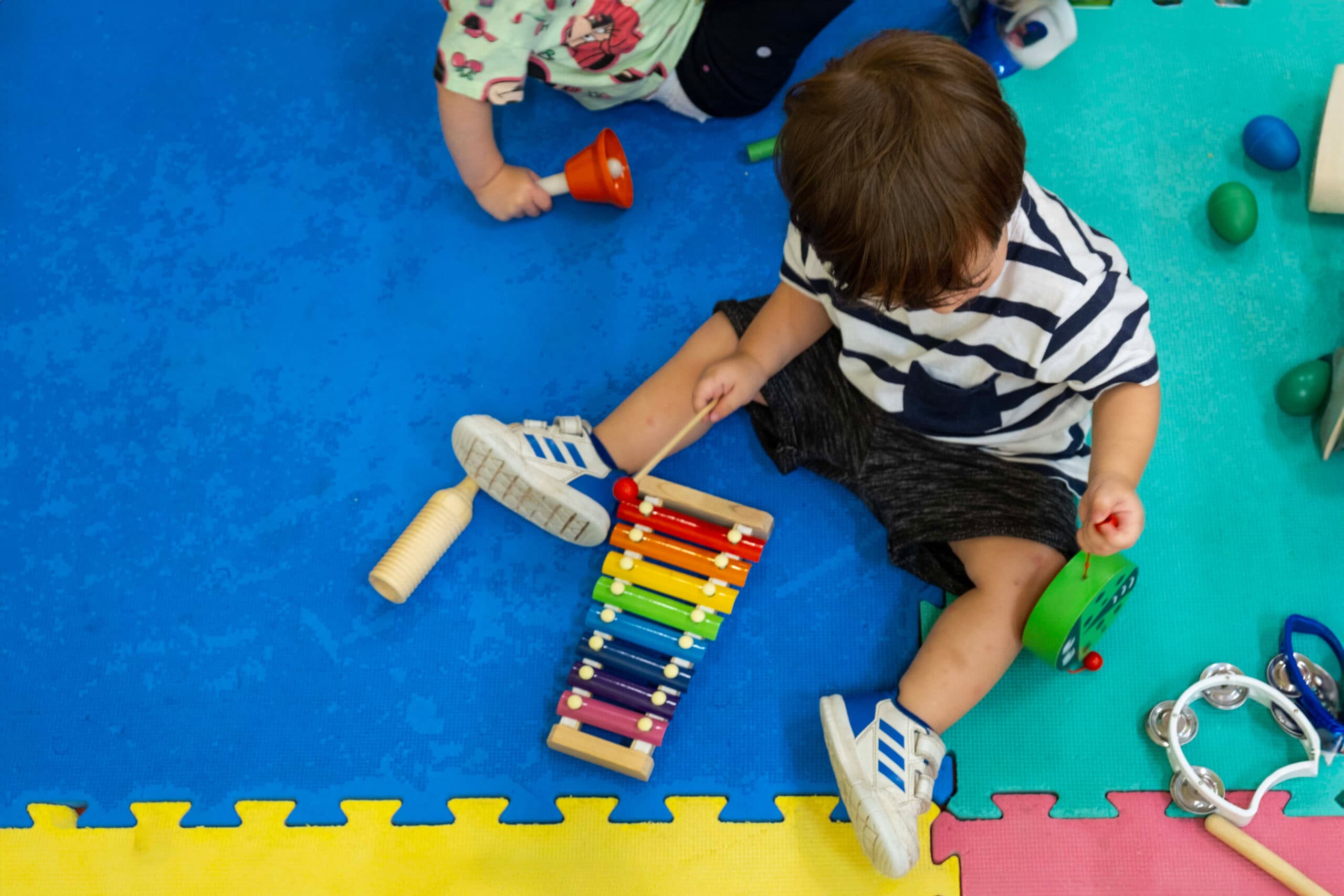 Menino a tocar xilofone, rodeado de outros instrumentos, na sala do infantário A Toca dos Traquinas